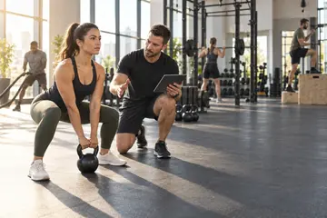 Personal trainer com tablet orienta aluna em exercício com kettlebell em academia iluminada