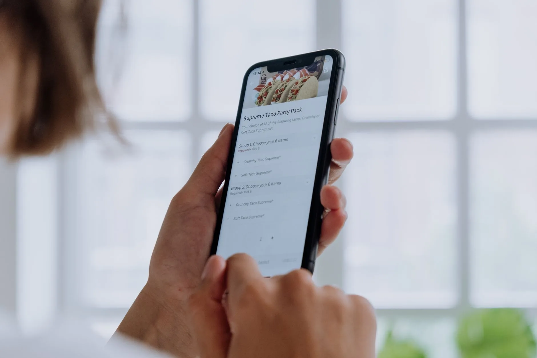 Mãos segurando um celular com um cardápio digital aberto para conferir um pedido